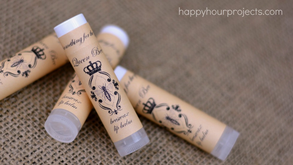 Four beeswax lip balm tubes wrapped in kraft paper Queen Bee labels lying together on a burlap cloth